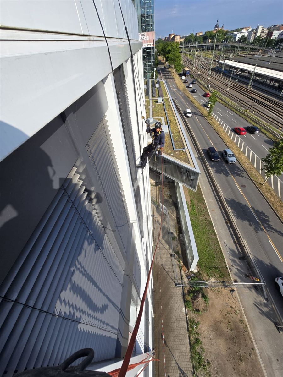 Industriekletterer in Mannheim reinigt Jalousien und Fenster an einer Bürofassade mit Blick auf die Bahngleise